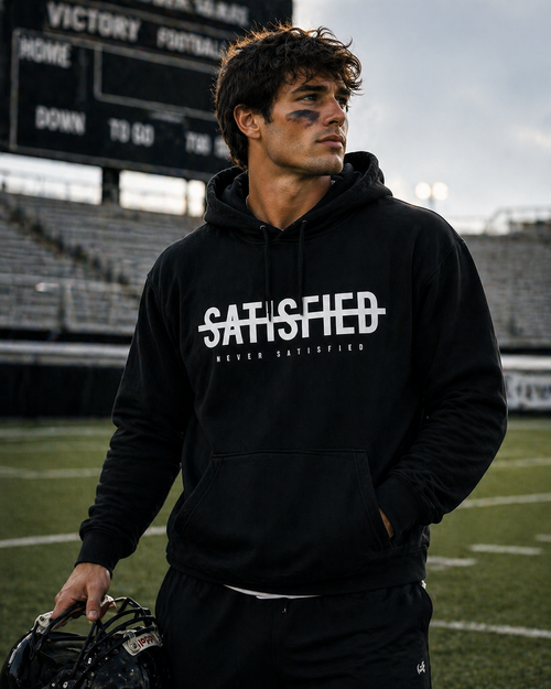 Black Never Satisfied hooded sweatshirt shown at a football field